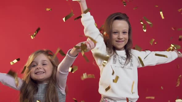 Pretty Little Girls Throwing Golden Confetti on the Red Background