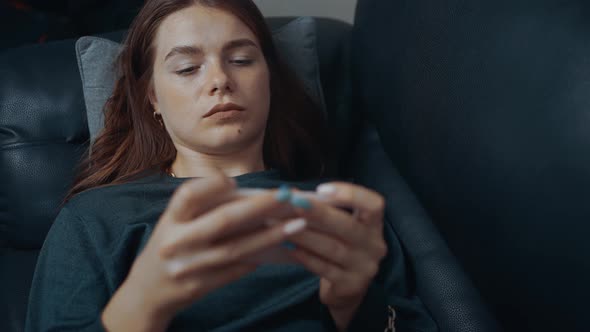 Redhead Freckled Playing Focused on the Phone Lying on the Black Sofa at Home