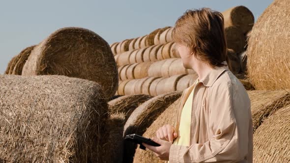 Farmer Agronomist Checks Hay Bales on the Wheat Field After Harvest at Sunset