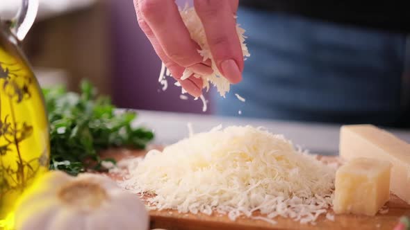 Woman Pours Grated Parmesan Cheese on Wooden Board at Domestic Kitchen