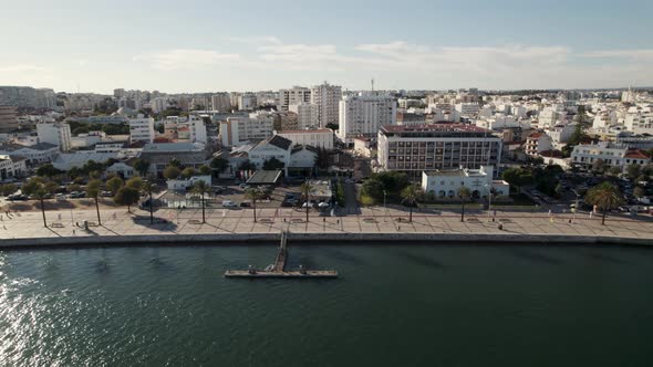 Aerial orbit over Portimão promenade, sun reflecting on Arade river, CIty buildings - Algarve