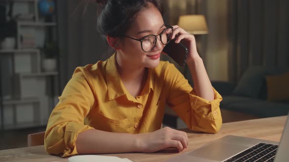 Young Asia Woman With Laptop Computer Calling On Smartphone From Home At Night