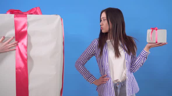 Young Asian Woman Gets a Huge Gift Instead of a Small Gift on a Blue Background