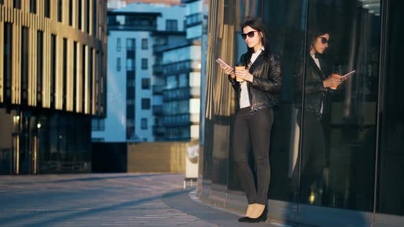 Young Attractive Businesswoman with Cup of Coffee is Using Smart Phone in the City with Office
