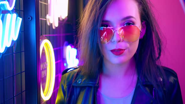 Mixed Raced Woman with Dreadlocks and Glasses Posing Near Glowing Neon Wall in the Dark