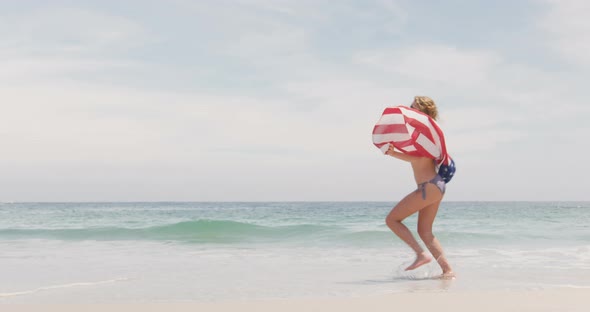 Side view of Caucasian woman with waving American flag running on the beach 4k