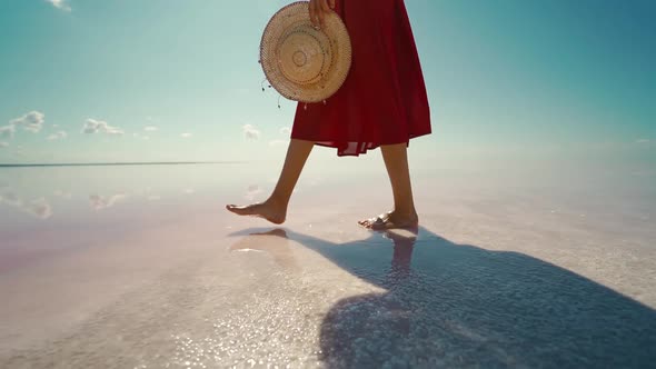 Side View Woman Legs in Red Skirt Walking on Salt White Beach Holding Straw Hat