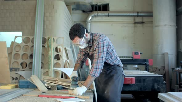 Bearded Carpenter in Safety Glasses Working with Electric Planer in Workshop