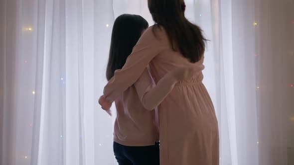 Back View Girl Looking Out Window Waiting for Santa As Woman Entering Living Room Hugging Child