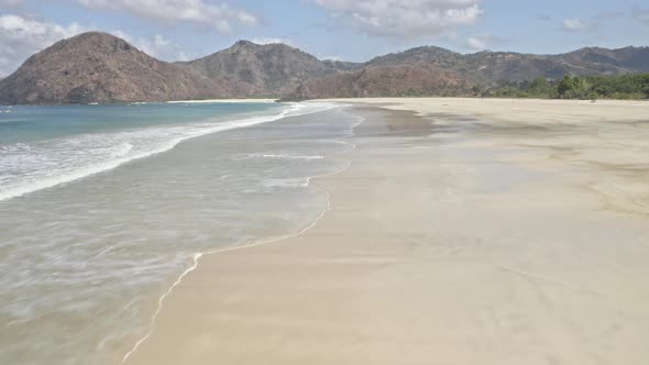 Drone Hovering Above Beach Shore, Waves and Glimpse of Mountain and Sky