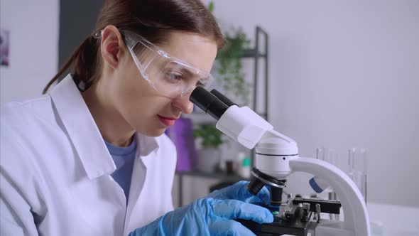 Young Woman Scientist is Examining Samples Under Microscope