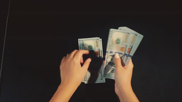 Woman Hands Count Earnings a Pack of Dollars on the Black Background