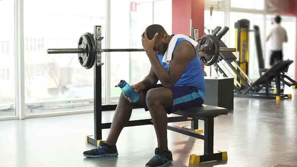 Upset African-American Sportsman Sitting on Training Equipment at the Gym