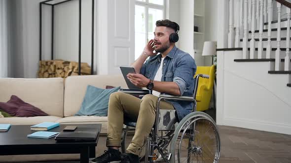 Bearded Guy in Wheelchair which Having Fun Alone while Enjoying Dancing Music in Headphones at Home