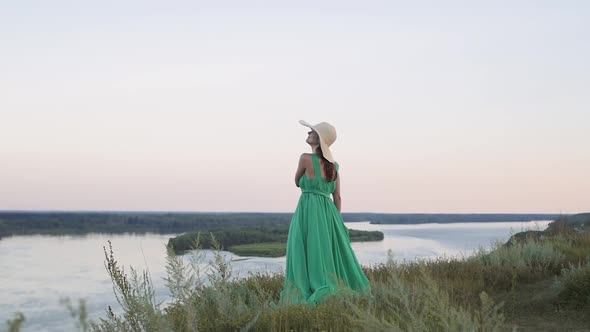 Young Woman in a Green Dress Posing on the Background of a Beautiful Landscape