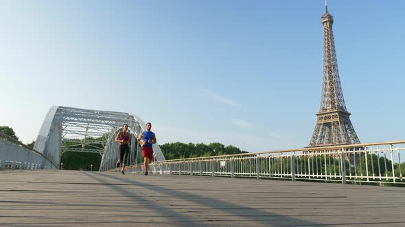 A man woman couple running across a bridge with the Eiffel Tower