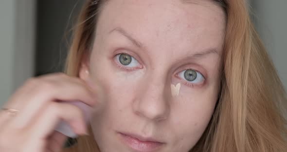 Woman applying eye conciliar with make up sponge.