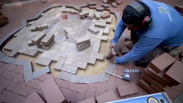 Hardscaping expert wearing ear protection uses a rubber mallet to fit a custom cut brick into place.