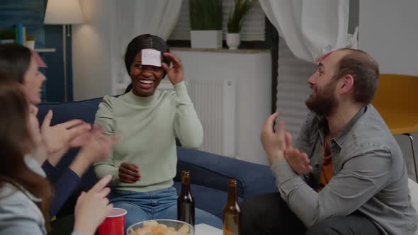 Multiracial Friends Playing Guess Who Game with Sticky Papers Attaching on Forehead