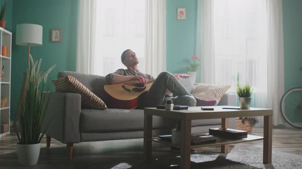 Young Man Is Playing Guitar Sitting On Sofa