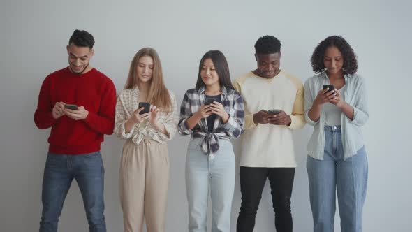 Group of Young Cheerful Diverse Friends Web Surfing on Smartphones Watching Social Media and Sharing