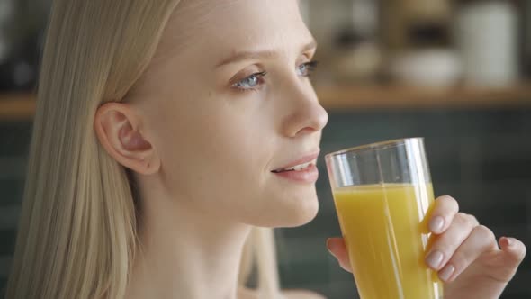 Young Woman Drinks Orange Juice From a Glass in the Kitchen Closeup