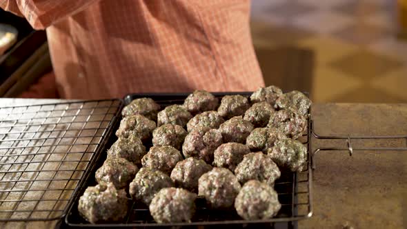 Man rolls balls of kofta in his hand and puts into grilling basket for cooking.  Camera slides from