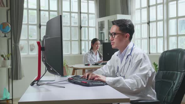 Young Asian Man Doctor Is Using Desktop Computer In Workplace. Medical Concept