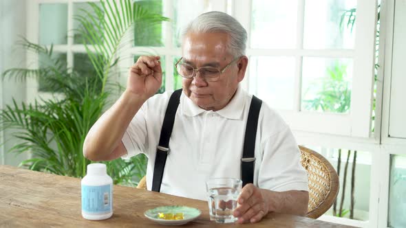 Elderly Asian Man Taking Pill with Cup of Water at Home