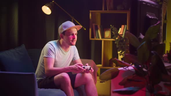 Young Man Sitting on Sofa and Playing Video Game on TV in Living Room