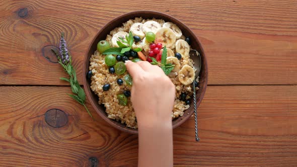 Wholegrain Oatmeal porridge with fresh berries, fruits nuts mint leaves sesame seeds in child hands