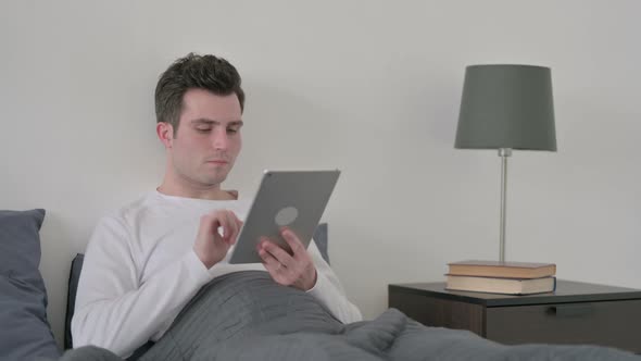 Man Using Tablet While Sitting in Bed