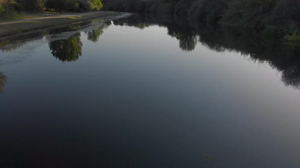 Drone shot of a calm river surrounded by trees during sunset