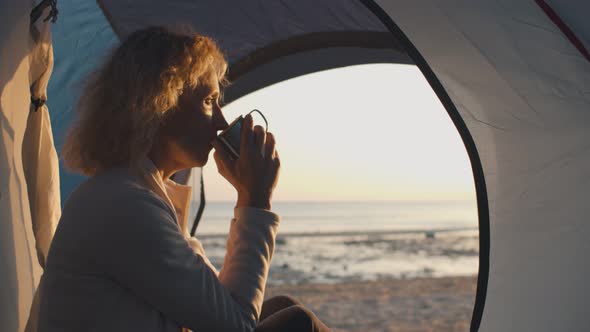 Portrait of Camping Mature Happy Woman Sitting in Tent Drinking Tea and Enjoying Sunset on Beach