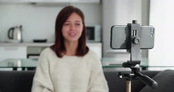 Tracking Shot with Rack Focus of Young Female Video Blogger in a Sweater Talking to Camera When