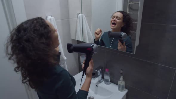 Positive Black Woman Singing in Handheld Dryer As Microphone Indoors