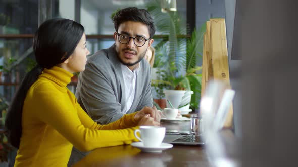 Asian and Middle Eastern Coworkers Talking and Using Laptop in Cafe