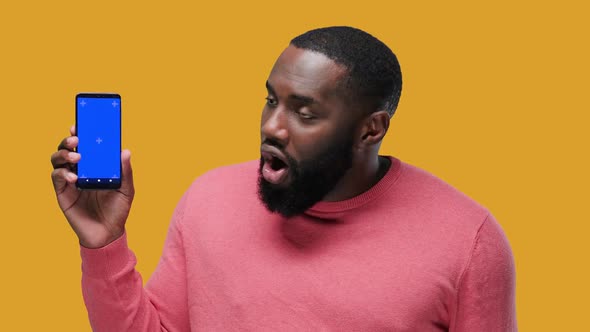 Happy Young Black Guy Showing His Phone Screen with Chroma Key and Pointing to It on Yellow