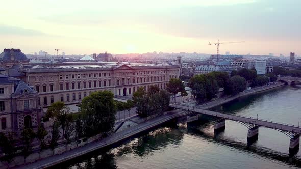 Morning aerial footage of Louvre museum and Pont des Arts bridge over Seine river. Drone flying down
