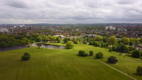 Reversing reveal over the lush green grass and a duck pond in Clapham Common