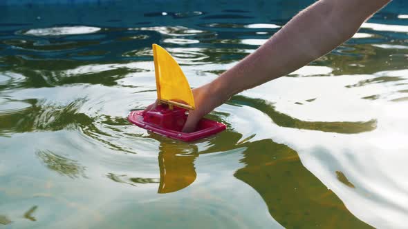 Hand of a Young Man Drowns a Toy Ship