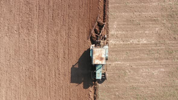 Top aerial view of tractor plowing ground on agriculture farm field.