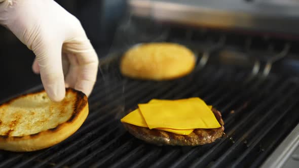 Hands of a person fry buns on grill. Meat cutlet with cheese on top. Fast food concept.