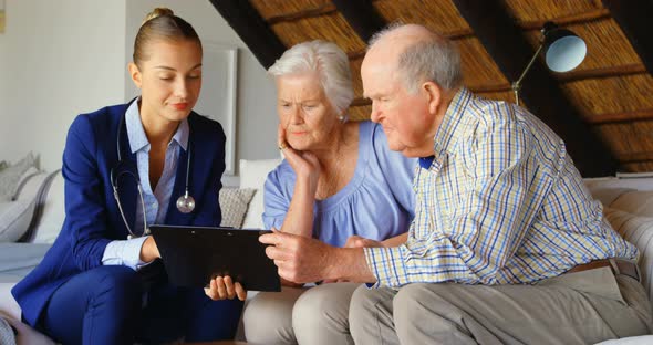 Front view of Caucasian senior couple discussing over clipboard with female doctor at comfortable co