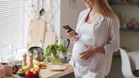 Pregnant Woman Messaging on Smartphone in Kitchen