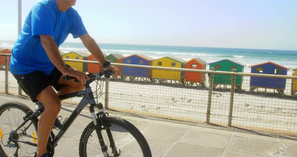 Side view of active senior Caucasian man riding bicycle on a promenade at beach 4k