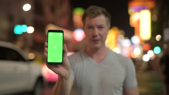 Young Happy Tourist Man Showing Phone Against View of the Streets in Chinatown at Night