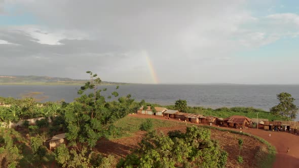 Aerial shot flying over a poor village in Africa with a rainbow over lake Victoria in the background
