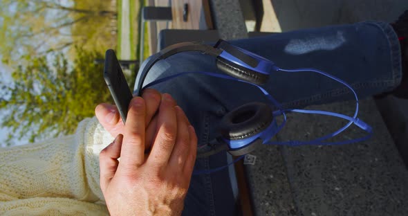 Hands of a Mature Man with Smartphone and Headphones  He Chatting with Friends Outdoor