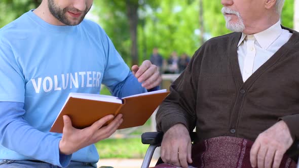 Male Volunteer Reading Book to Lonely Disabled Pensioner in Park, Social Support